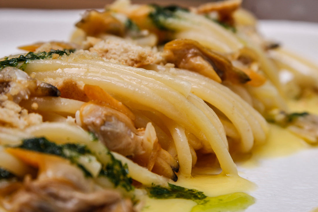 Spaghettoni alle vongole serviti su riduzione di datterino giallo con taralli sbriciolati e pesto di prezzemolo